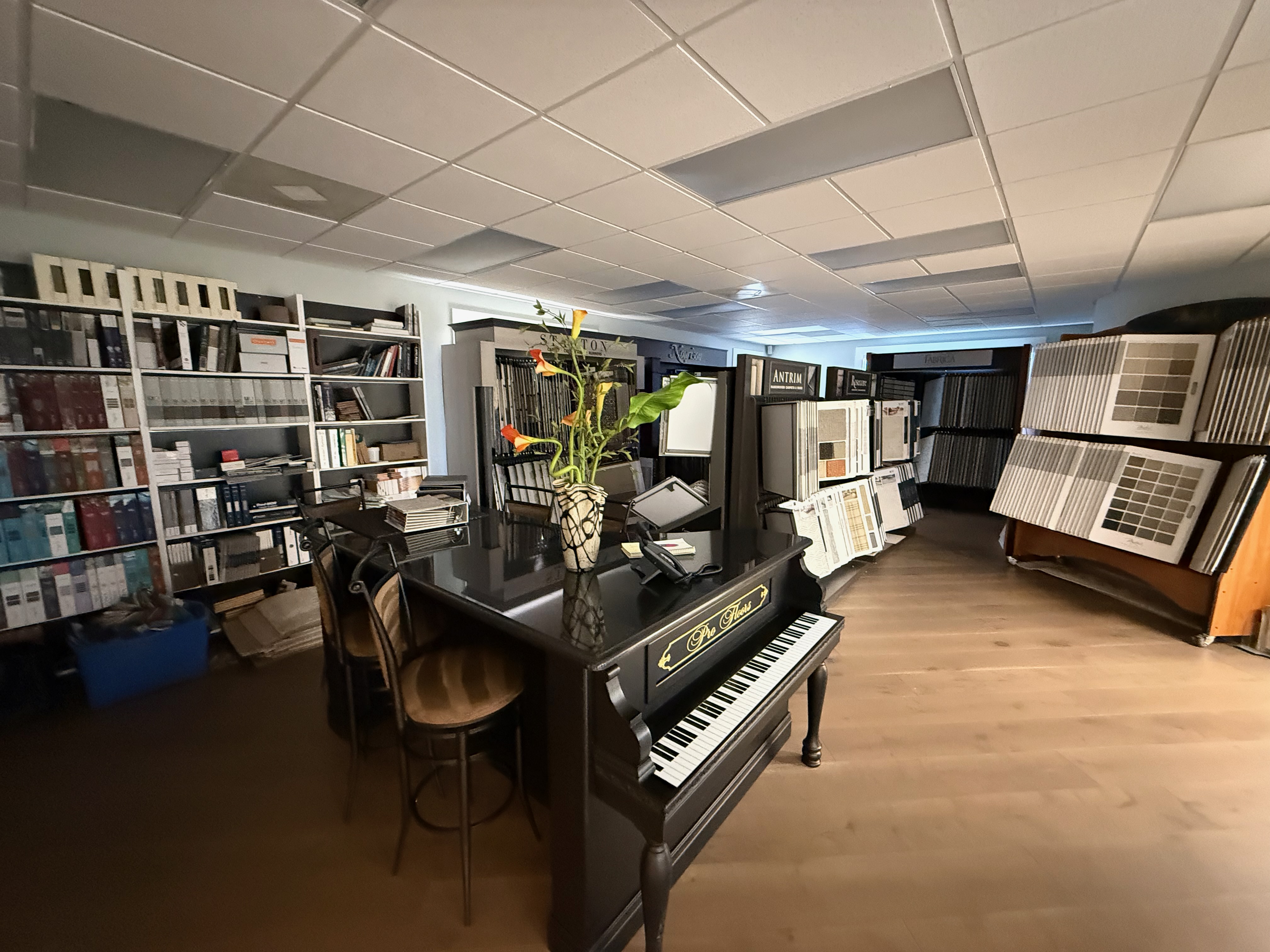 The custom-bind broadloom room in the Naples showroom — wool rolls and bound rugs anchored by the antique grand piano