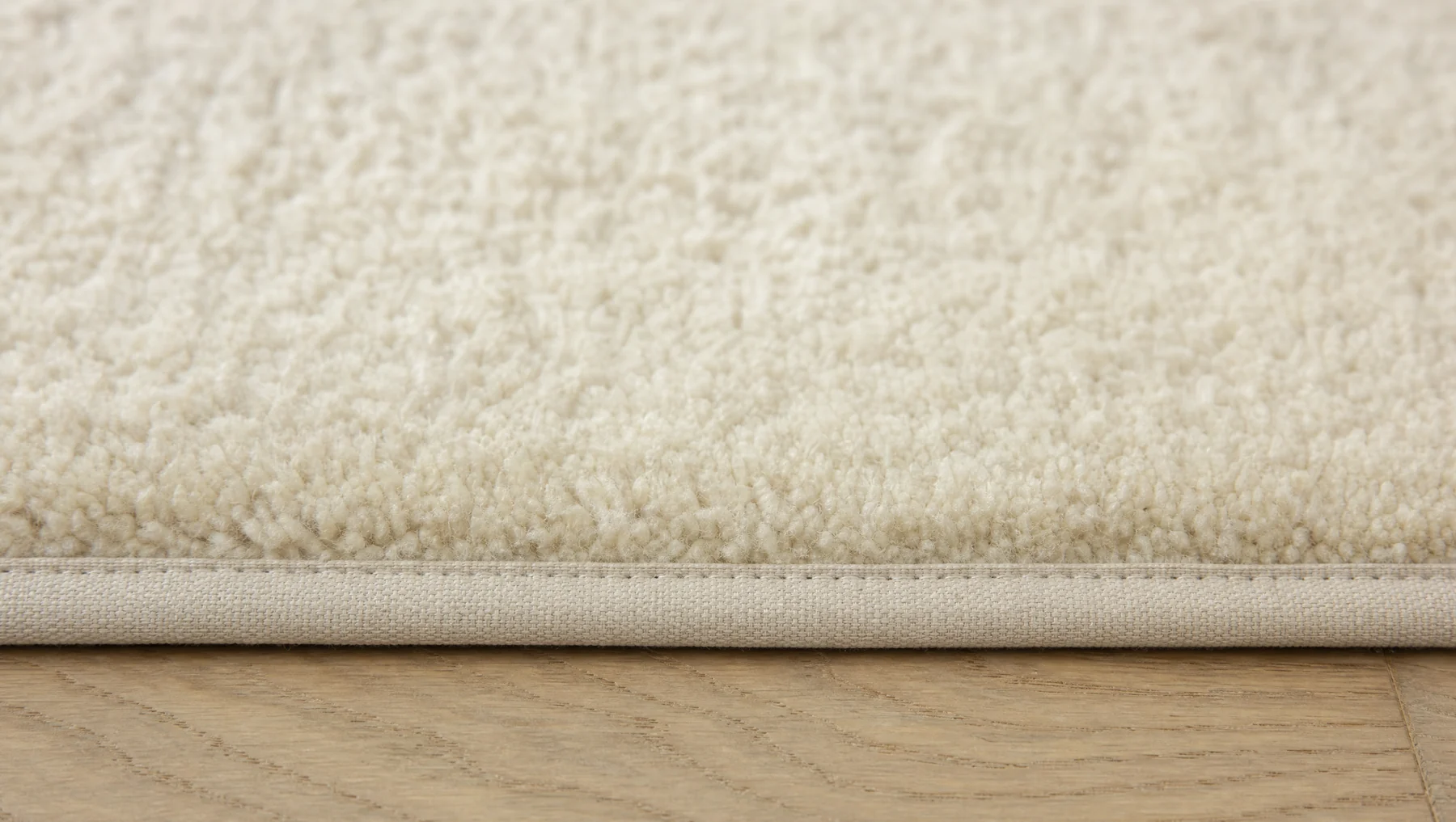 Cut-pile carpet with a cotton bound edge, shown where it meets a wood floor