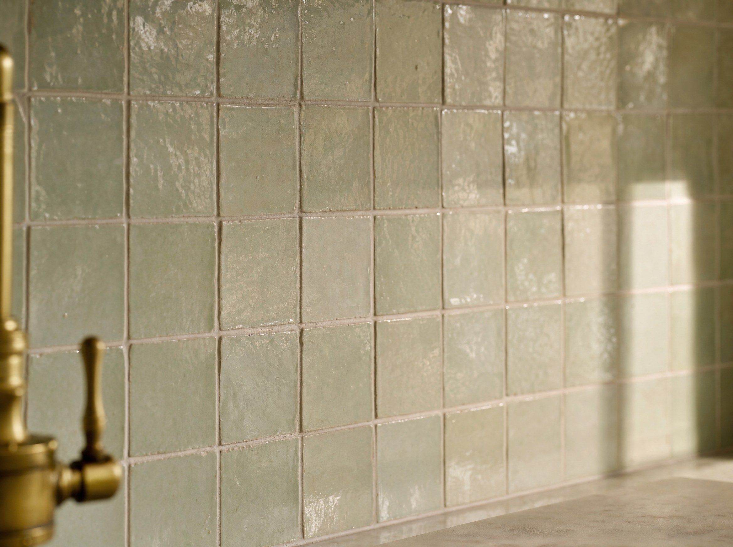 Handmade glazed zellige backsplash in a soft sage glaze catching warm light — representative rendering