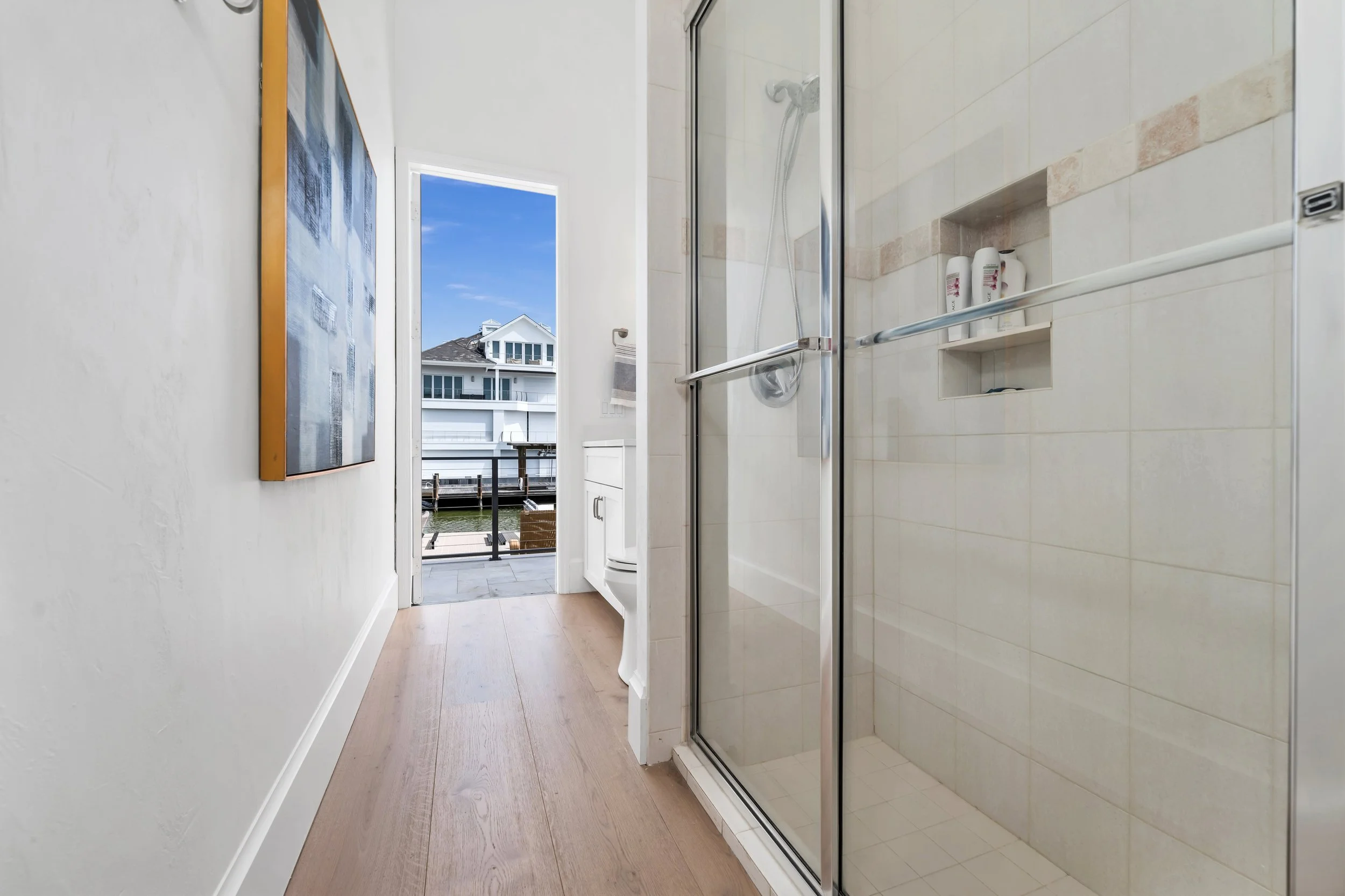 Naples guest bath with a field-tile shower and an accent band, beside an oak-floored hall